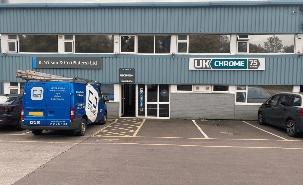 Exterior of the UK Chrome building featuring signage for R. Wilson & Co (Platers) Ltd and UK Chrome's 75th anniversary. A blue CJ Signs van with ladders on top is parked in front of the building near the main entrance, which has a 'Reception' sign above it. Other parked cars are visible to the right.